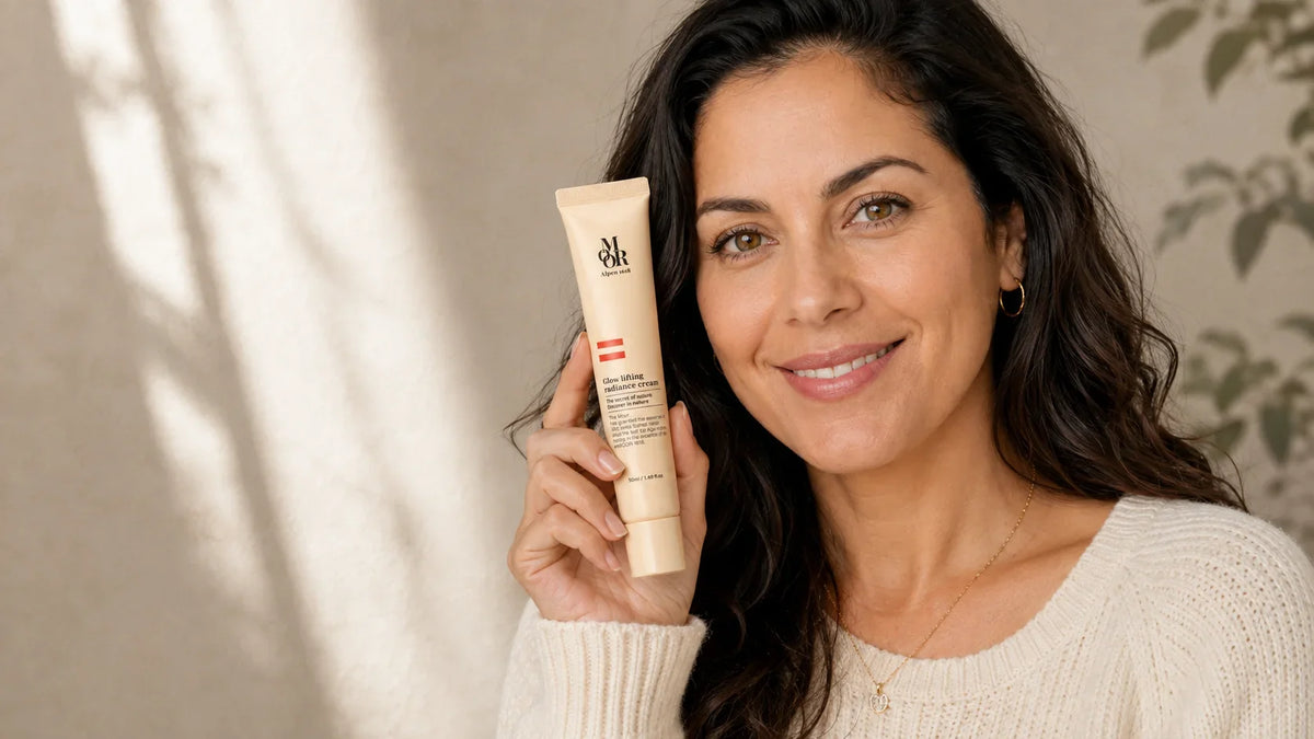 Smiling woman in her 40s holding an Alpen MOOR 1618 Glow Lifting Radiance Cream tube beside her face