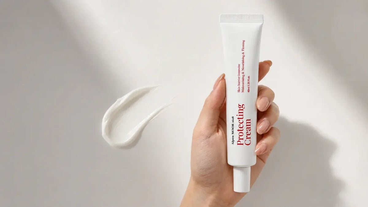 Hand holding an Alpen MOOR 1618 Protecting Cream tube beside a smoothed swatch of the cream